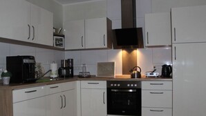A modern kitchen with white cabinets, a built-in oven, a coffee maker, and a kettle. - An der Muhlenbachaue (Nettetal)