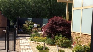 A garden with a paved walkway, potted plants, and a brick building. - An der Muhlenbachaue (Nettetal)