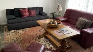 A living room with a black sofa, a red sofa, a wooden coffee table, and a patterned rug. There are three framed pictures on the wall. - An der Muhlenbachaue (Nettetal)
