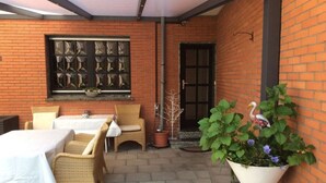 An outdoor patio with wicker furniture, a white tablecloth-covered table, and a potted plant with flowers. - An der Muhlenbachaue (Nettetal)