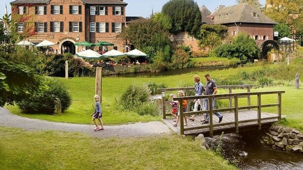 A historic building with a brick facade, a pond, and a wooden bridge. - An der Muhlenbachaue (Nettetal)