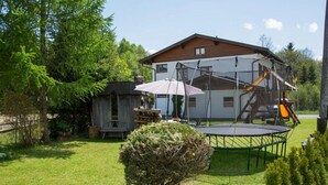 Ein Haus mit Trampolin, Schaukel und einer kleinen Gartenhütte auf einer Rasenfläche.