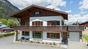 Eine zweistöckige Chalet mit Balkon, Steinuntergrund und einer Garage.