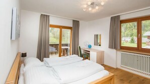 Ein Schlafzimmer mit einem hölzernen Bett, einem Schreibtisch, einem Stuhl, einer Heizung und großen Fenstern mit Vorhängen.