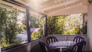 Un espacio de estar techado al aire libre con una mesa y sillas, con vistas a un cuerpo de agua y vegetación.