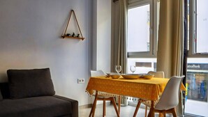 A modern living room with a sofa, dining table with chairs, and a window with curtains. - Apartment in Conil Near Scenic Beaches (Conil de la Frontera)