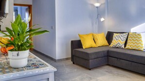 A modern living room with a grey sectional sofa, yellow and patterned cushions, a potted plant, and a tiled coffee table. - Apartment in Conil Near Scenic Beaches (Conil de la Frontera)