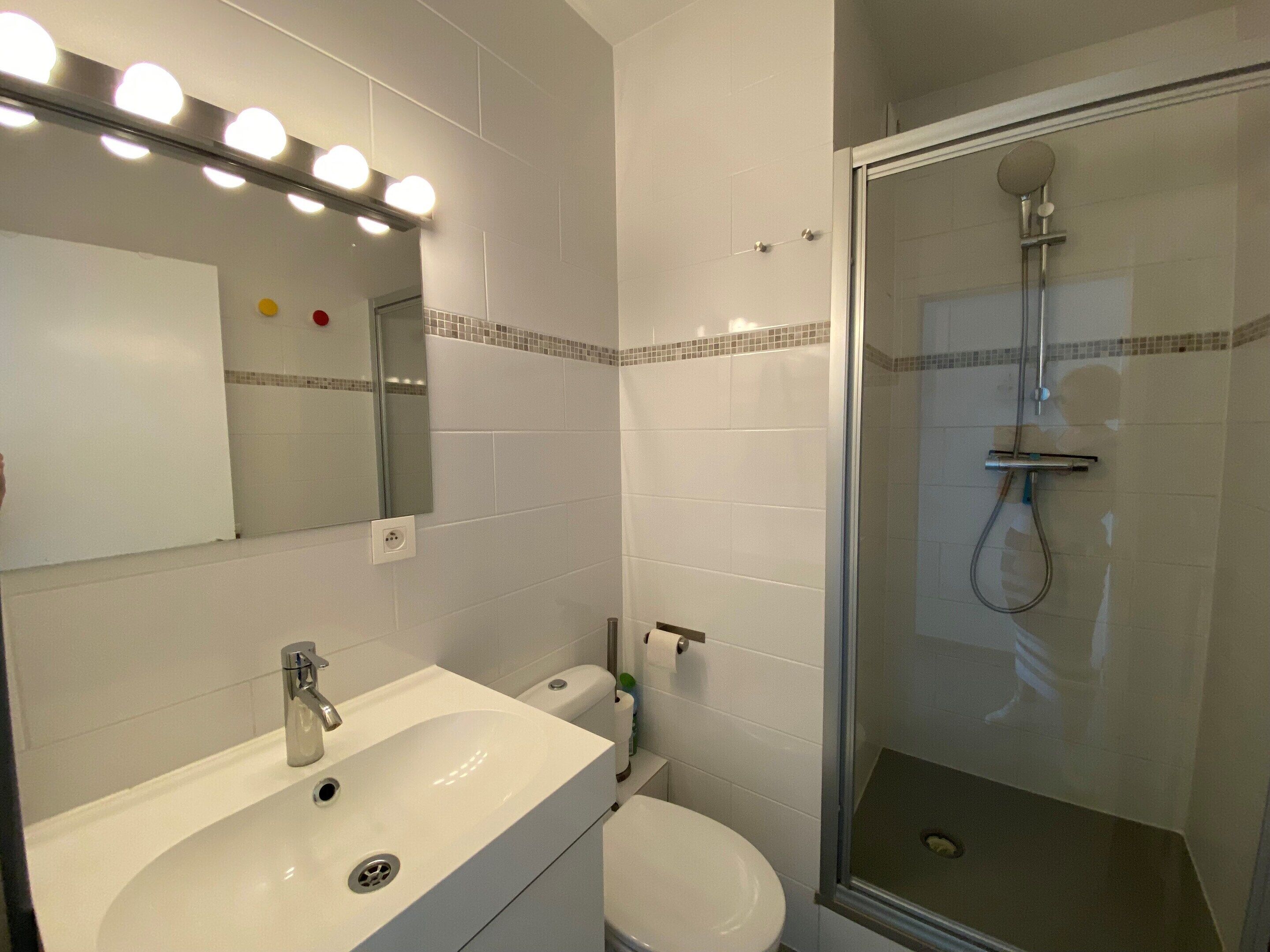 A bathroom with a white sink, mirror, and shower.