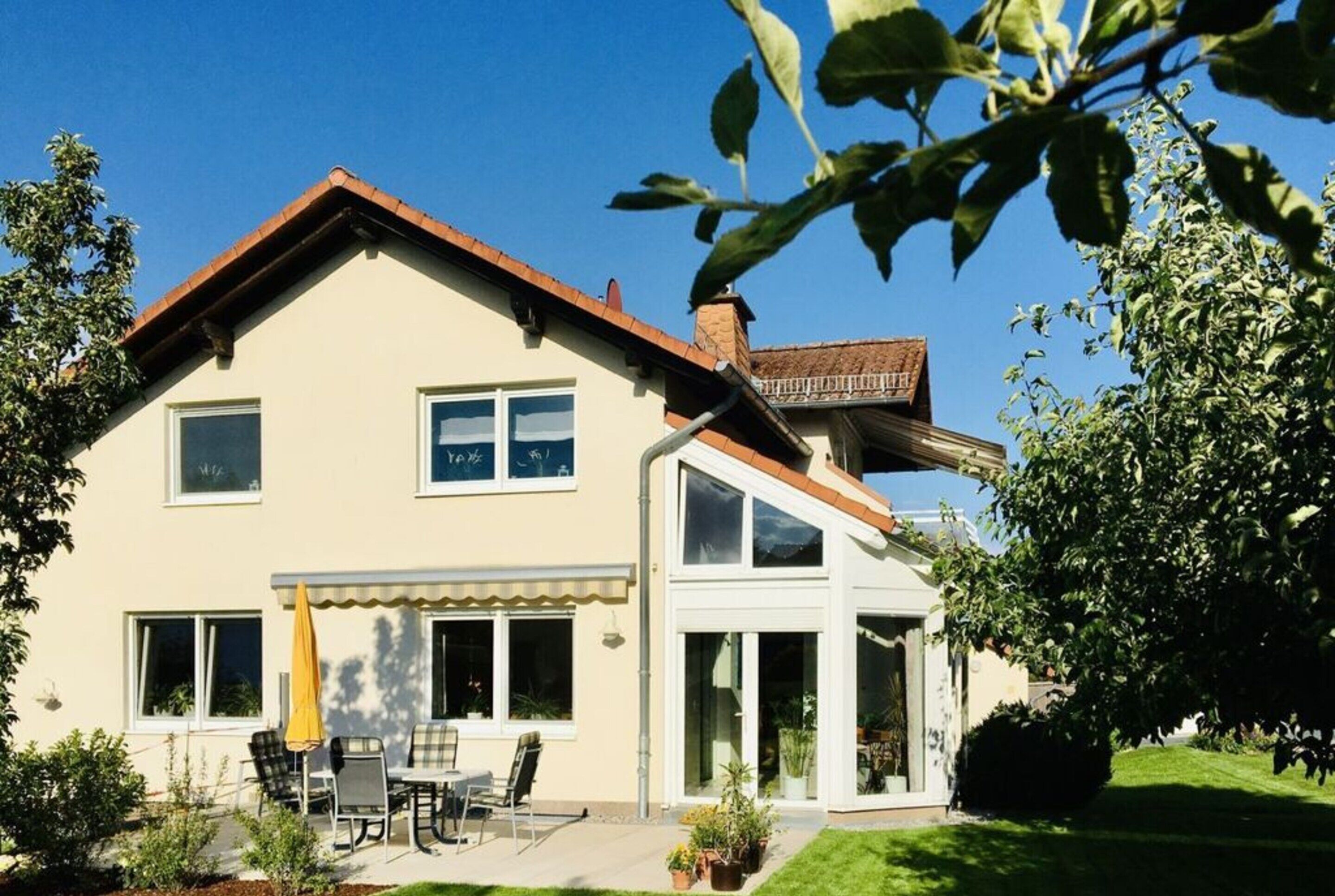 Ein zweistöckiges Haus mit Terrasse, Essbereich und Wintergarten.
