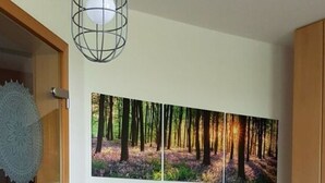 A dining area with a wooden table, two blue chairs, a white candle with an anchor design, and a forest-themed wall art. - Apartment in Rieseby (Rieseby)