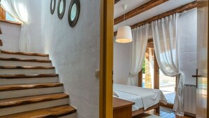 Un dormitorio con una escalera de madera, una cama, una mesita de noche y un ventanal con cortinas.