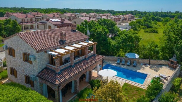 Una amplia casa de piedra con tejado de tejas, piscina y jardín cuidado.
