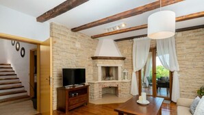 Una sala de estar con chimenea de piedra, vigas de madera, televisor y sofá.