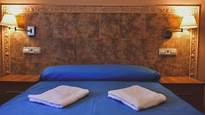 A hotel room with a large bed, two nightstands, and two wall-mounted lamps.