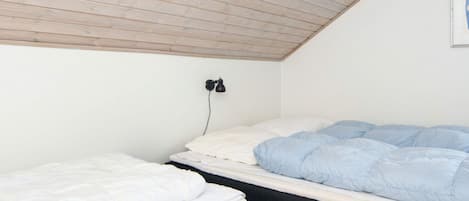 A room with two beds, one with a white mattress and the other with a blue one. There is a black wall-mounted lamp on the wall.