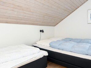 A room with two beds, one with a white mattress and the other with a blue one. There is a black wall-mounted lamp on the wall. - 4 Star Holiday Home in Romo (Rømø)