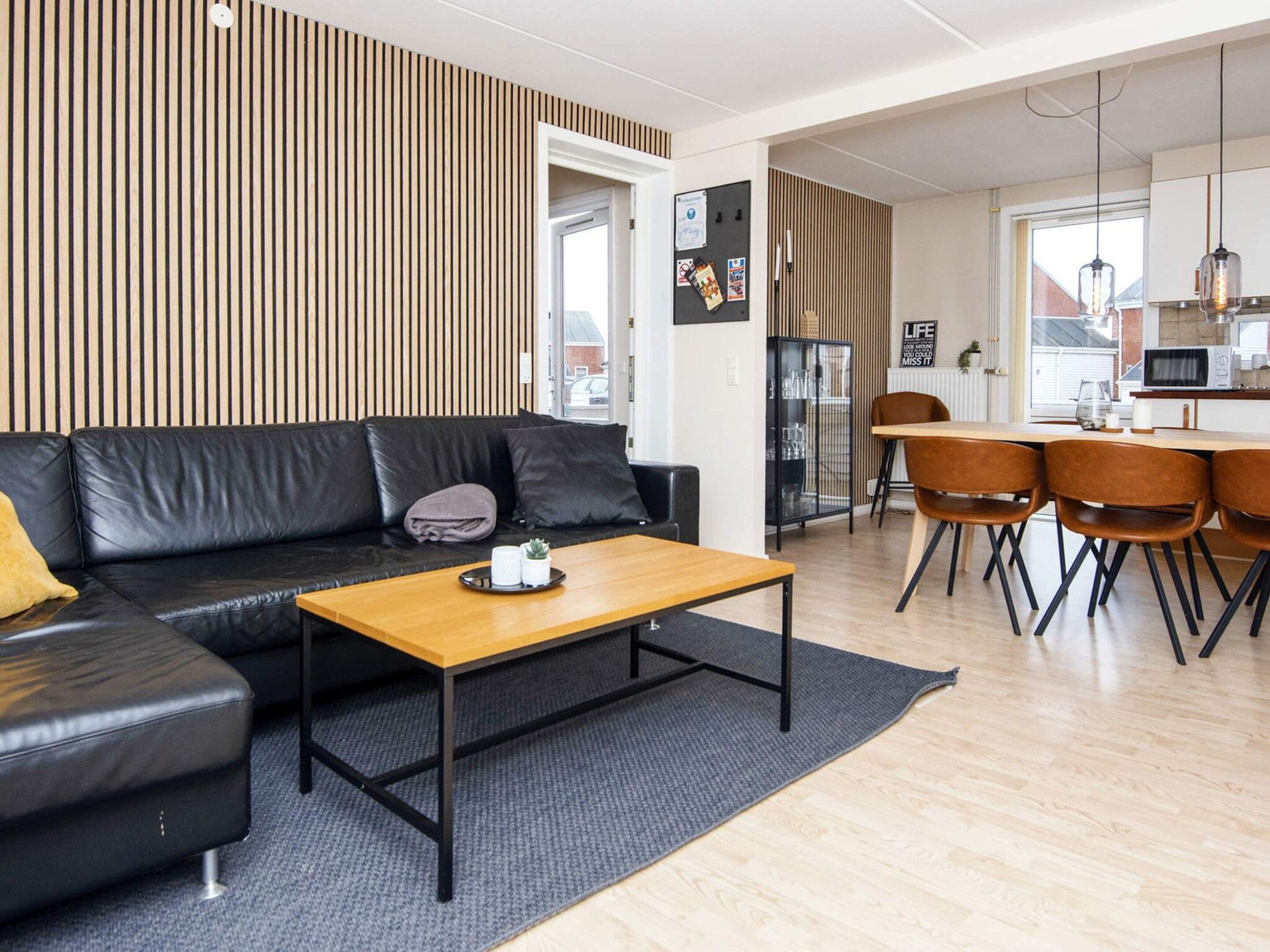 Ein modernes Wohnzimmer mit einem schwarzen Ledersofa, einem Holztisch und einem Essbereich mit einem Holztisch und vier Stühlen.