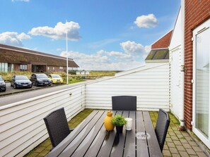 A patio with a table and chairs, a yellow car parked on the street, and a building in the background. - 4 Star Holiday Home in Romo (Rømø)