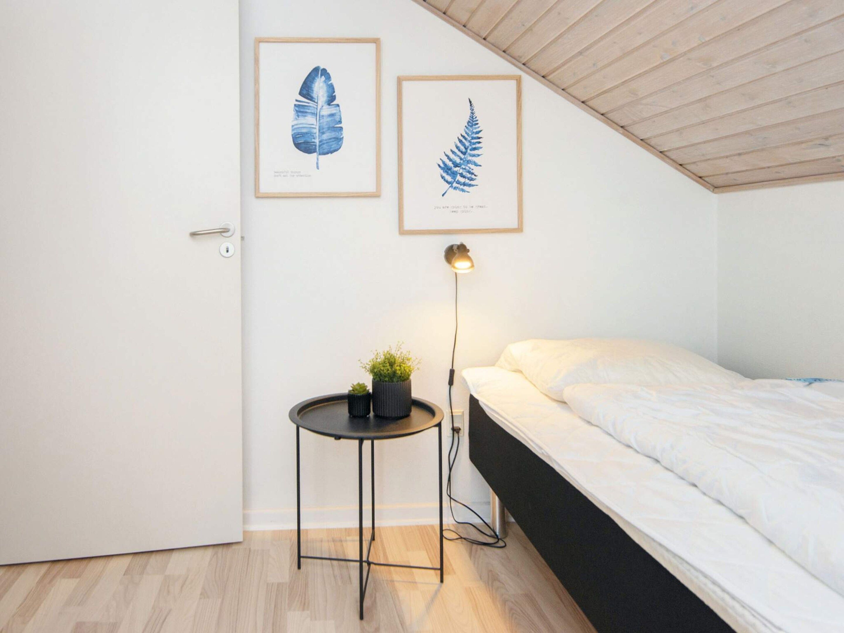 Ein Schlafzimmer mit einem Bett, einem Nachttisch mit Lampe und zwei gerahmten Pflanzenbildern an der Wand.