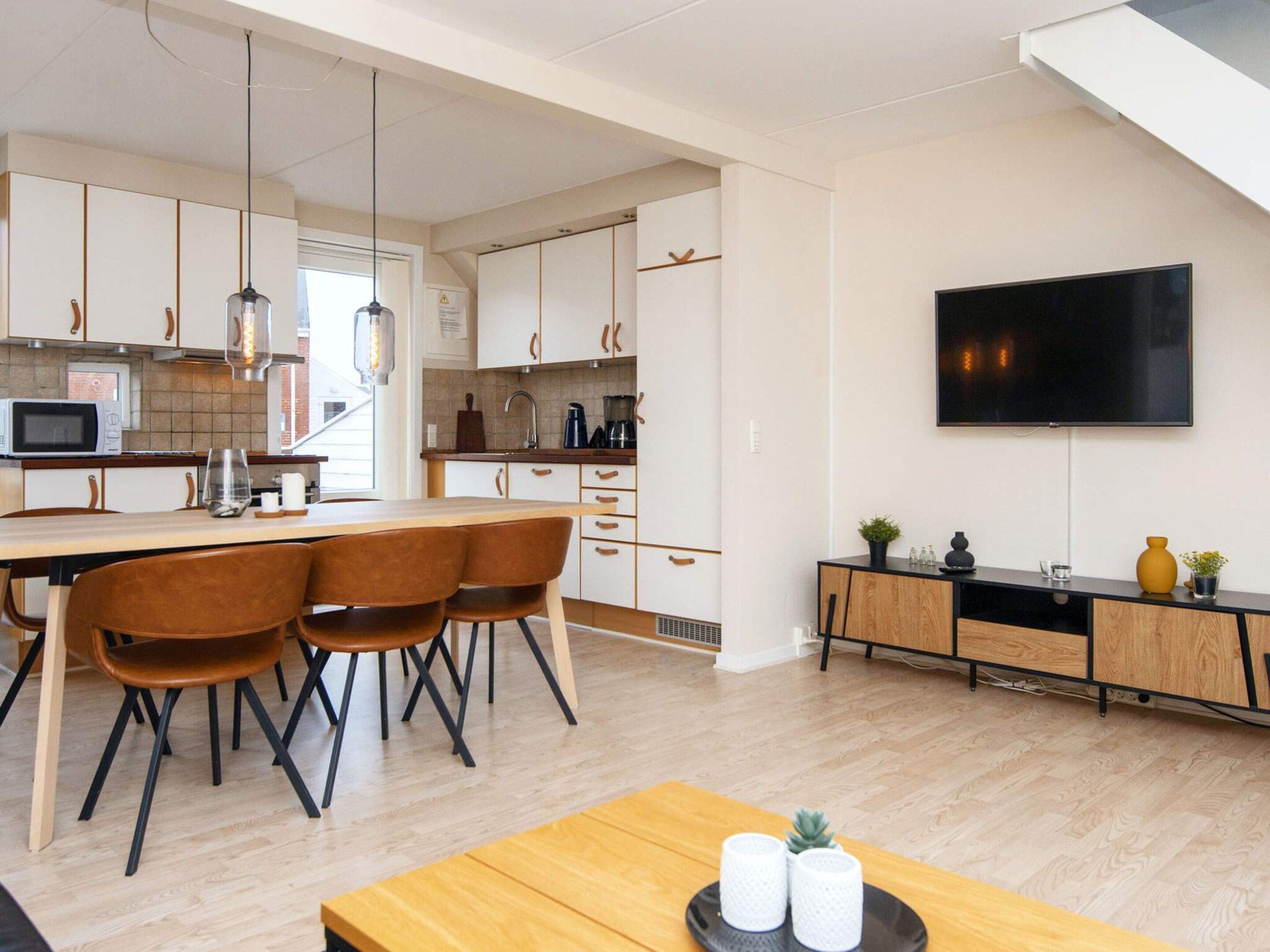 Eine moderne Küche mit Essbereich, einem Flachbildfernseher an der Wand und einem Holztisch mit Stühlen.