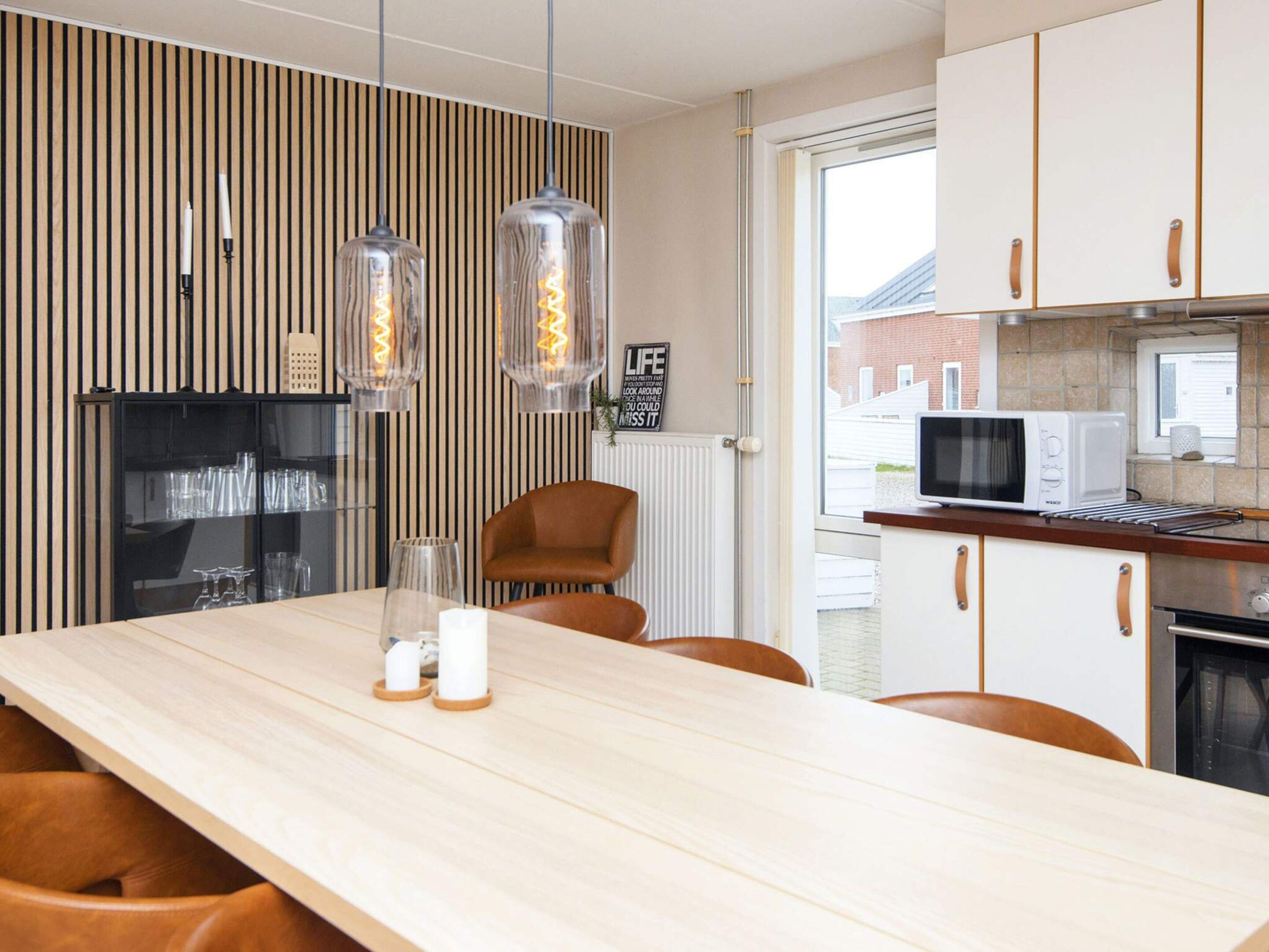 Een moderne keuken met een houten tafel, twee hanglampen en een magnetron.