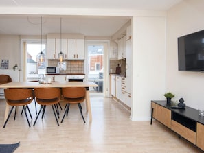 A modern kitchen with white cabinets, a dining area with wooden chairs, and a flat-screen TV mounted on the wall. - 4 Star Holiday Home in Romo (Rømø)