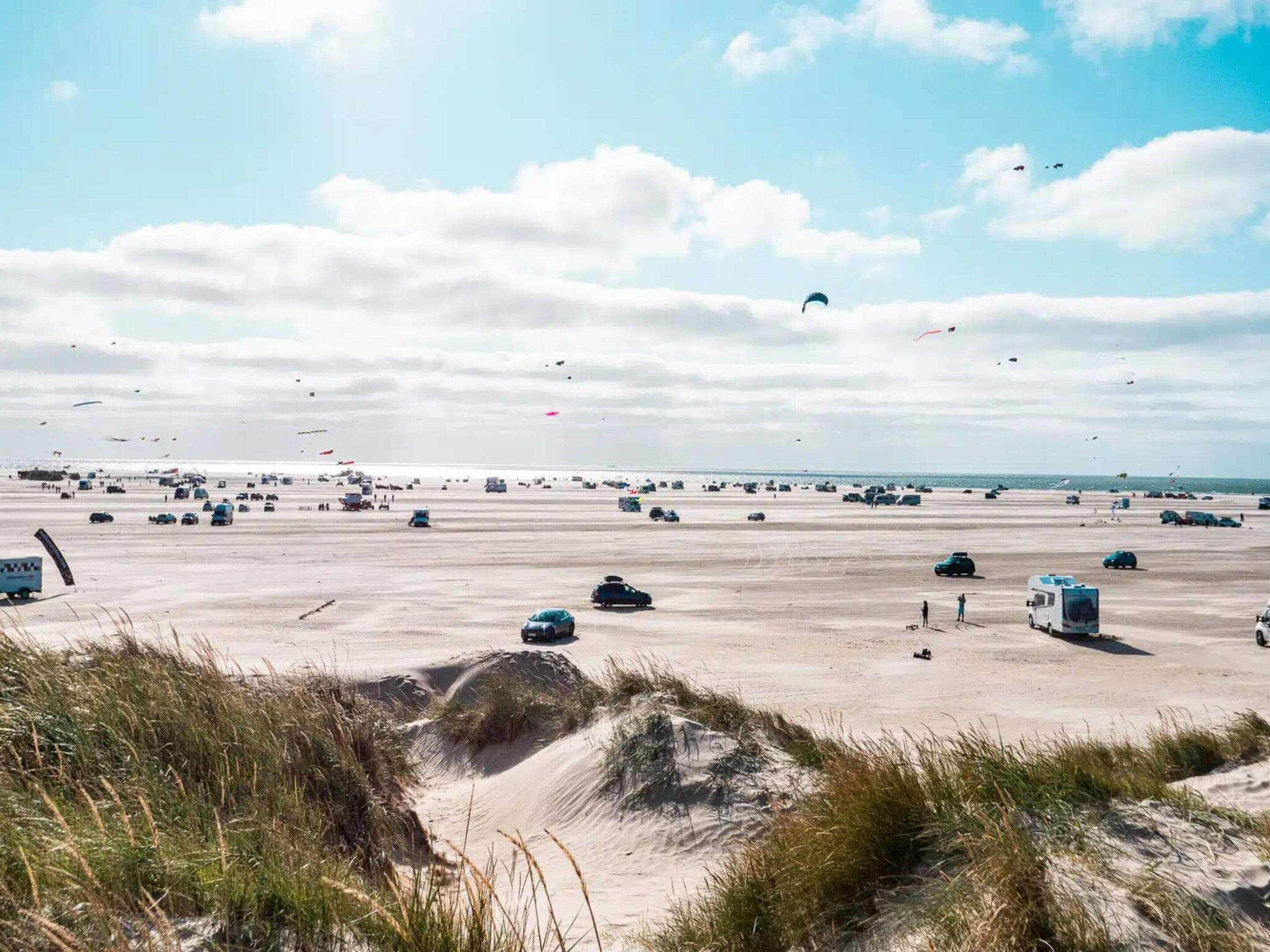 Une vaste étendue de sable, à ciel ouvert, où se trouvent quelques véhicules et quelques personnes, sous un ciel partiellement nuageux.