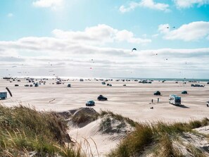 A wide, open sandy area with vehicles and a few people, under a partly cloudy sky.