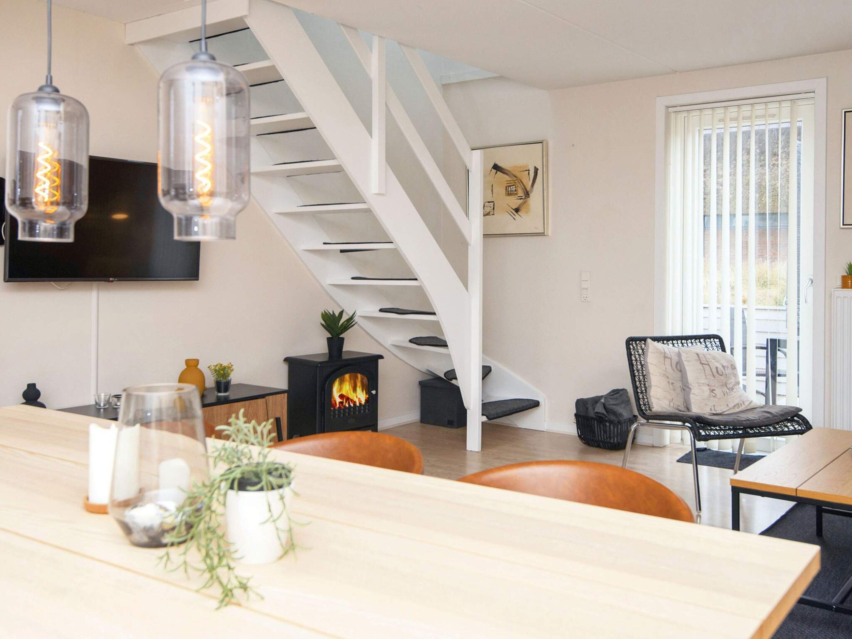 Ein modernes Wohnzimmer mit Treppe, Kamin, Esstisch und Wand-Fernseher.