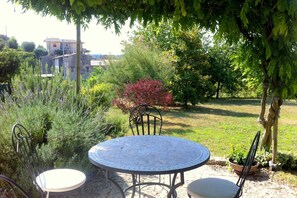 A round metal table with a white chair, surrounded by greenery and a building in the background. - Shimmering Serenity in Pastrengo (Pastrengo)