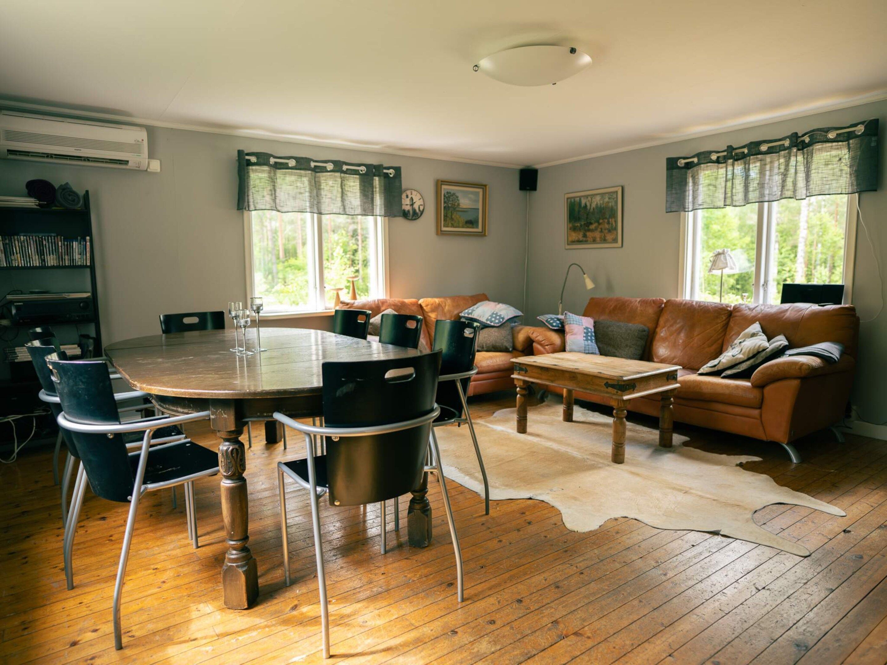 A cozy living room with a wooden dining table, leather sofa, and a cowhide rug.