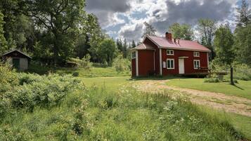 A red house with a red roof, surrounded by a grassy field and trees.