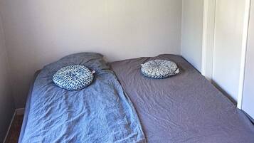 A small room with two single beds, each with a patterned pillow, grey bedding, and a painting on the wall.