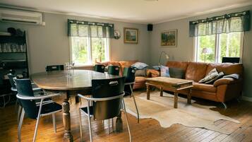 A cozy living room with a wooden dining table, leather sofa, and a large window with curtains.