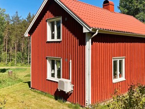 A red wooden house with a sloped roof, two windows, and an air conditioning unit attached to the side. - 6 Person Holiday Home in Sandhult (Sandhult)