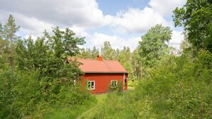 Une maison en bois rouge, entourée d’un feuillage vert et dense, sous un ciel dégagé.