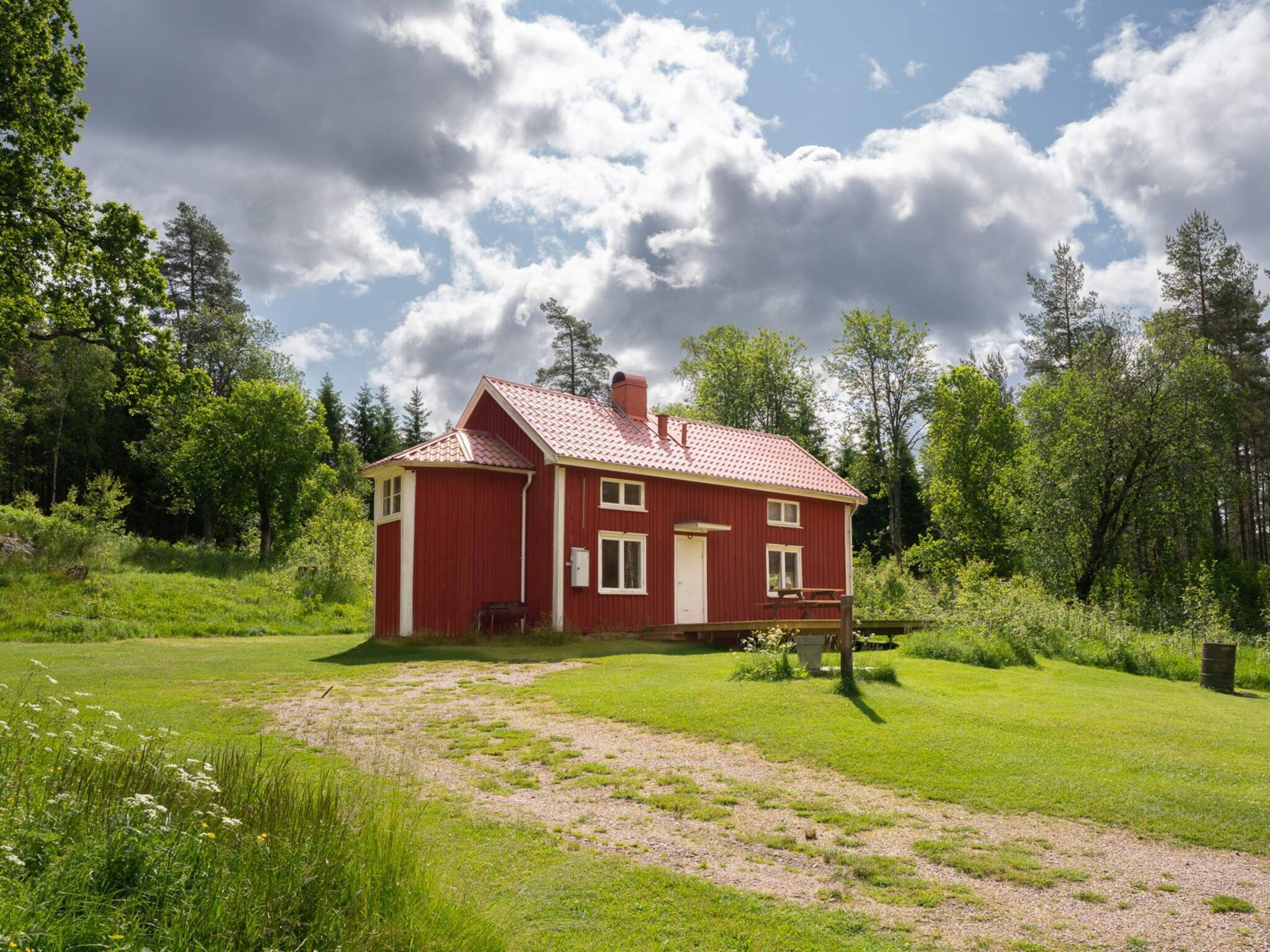 A red wooden house with a sloped roof, surrounded by a grassy field and trees.