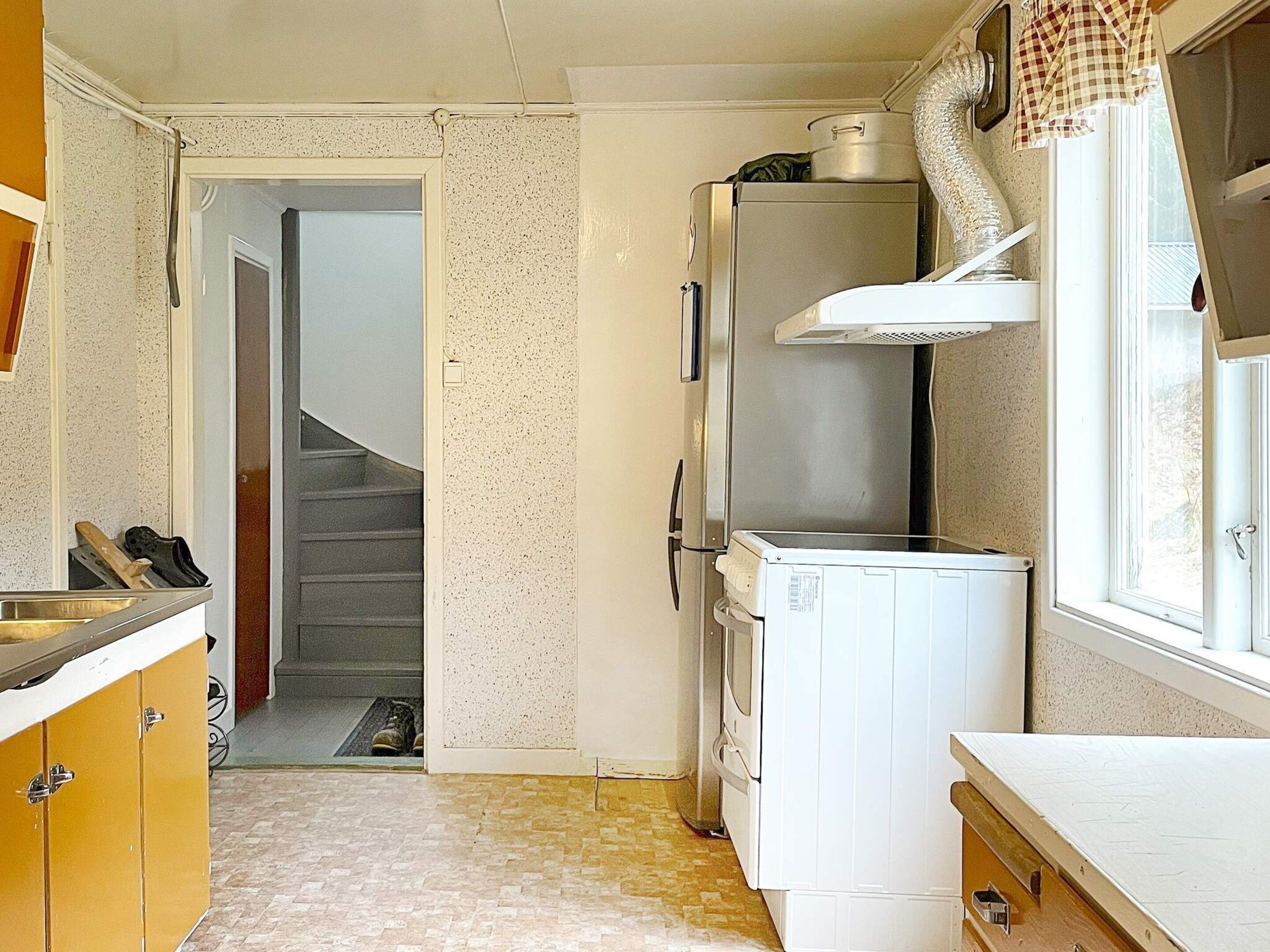 A compact kitchen with a refrigerator, a microwave, and a sink. There is a window with curtains and a door leading to another room.
