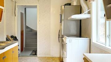 A compact kitchen with a refrigerator, a microwave, and a sink. There is a window with curtains and a door leading to another room.