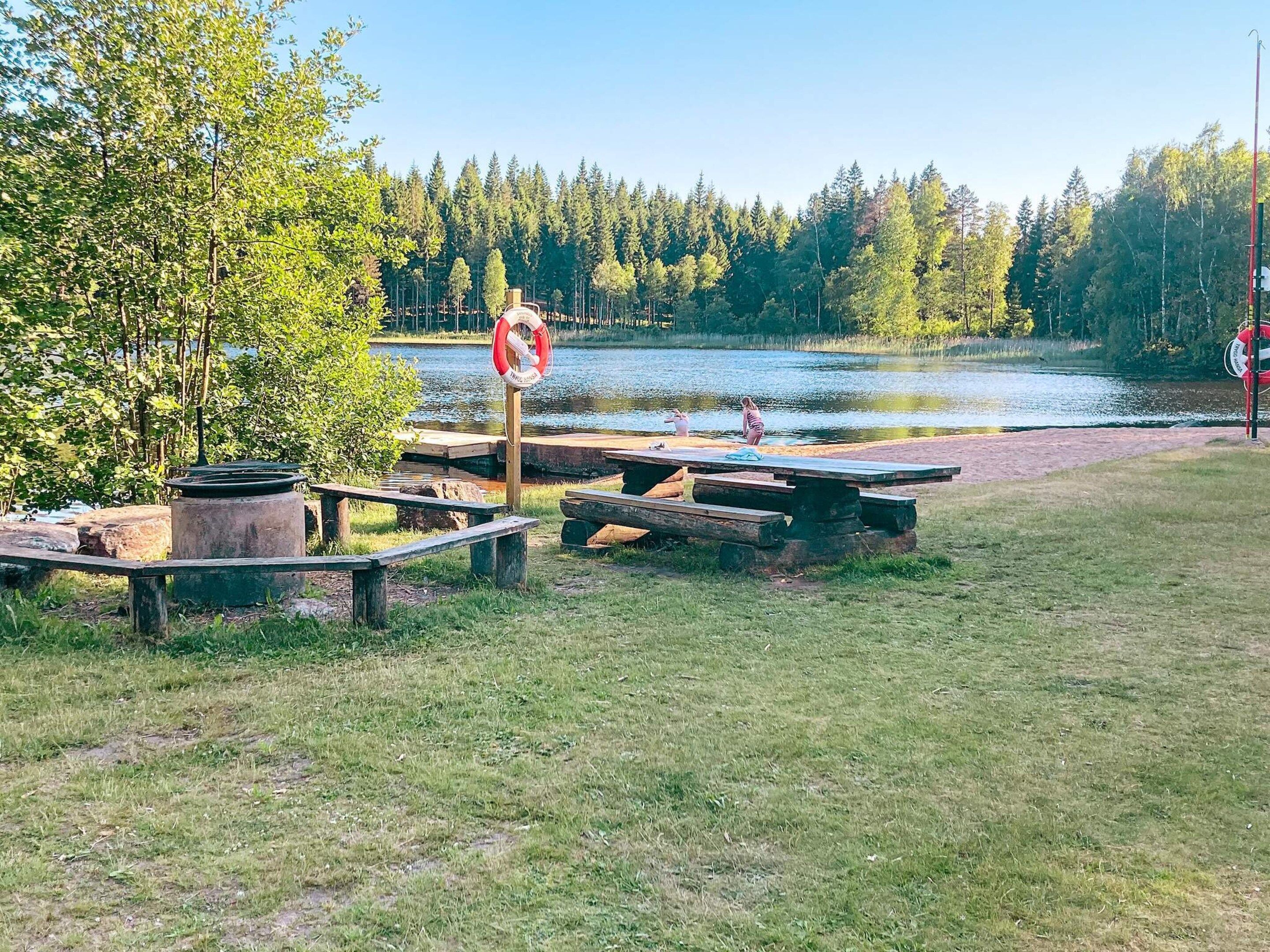 Un espace de pique-nique au bord du lac, équipé de bancs et de tables en bois, entouré d’arbres et offrant une vue dégagée sur le lac.