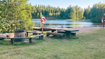 A lakeside picnic area with wooden benches and picnic tables, surrounded by trees and a clear view of the lake.