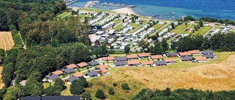 An aerial view of a coastal caravan park with rows of caravans and mobile homes, a marina, and a swimming pool complex.