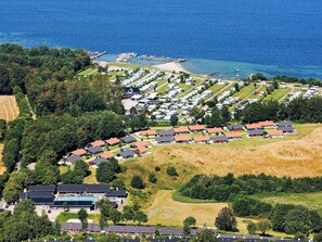 An aerial view of a coastal caravan park with rows of caravans and mobile homes, a marina, and a swimming pool complex.