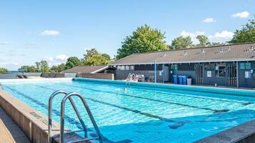 Una piscina con puesto de socorrista, sillas de descanso y una zona de estar cubierta.