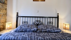 A bed with a metal headboard, two wall-mounted lamps, a framed picture on the wall, and a stone wall to the left.