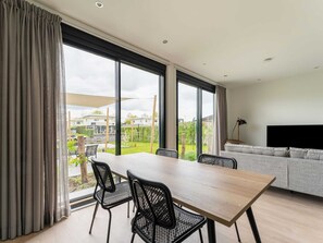 A modern living room with a large window, a dining table with chairs, a grey sofa, and a flat-screen TV. - Amazing Villa in Zeewolde With Terrace (Zeewolde)