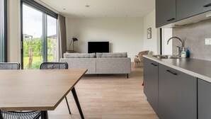 A modern living room with a sofa, a dining table, and a kitchen area with cabinets and a sink. - Amazing Villa in Zeewolde With Terrace (Zeewolde)