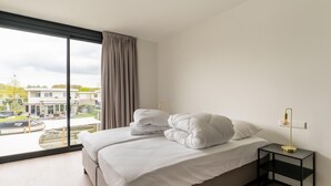 A modern hotel room with a large window, a bed with white linens, a black nightstand, and a view of the outside. - Amazing Villa in Zeewolde With Terrace (Zeewolde)
