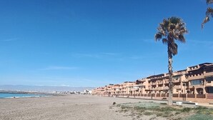 Un hôtel situé sur la côte, composé de plusieurs bâtiments à étages, avec une plage de sable fin et un ciel bleu dégagé.