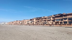 Une rangée de bâtiments beiges, à plusieurs étages et dotés de balcons, se dressant sur un paysage plat et aride, sous un ciel bleu dégagé.